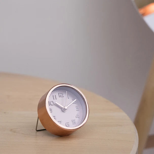 Copper-coloured Kikkerland mini alarm clock standing on a wooden table
