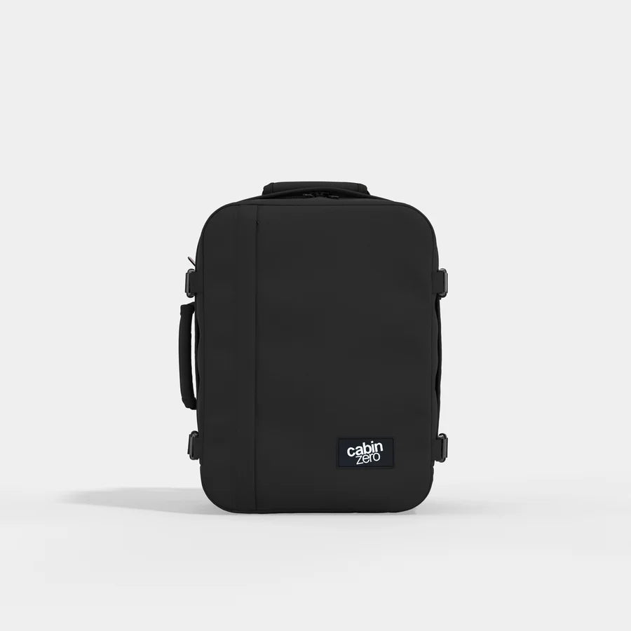 A black Cabin Zero backpack shown from the back, featuring a top handle, side compression straps, and a small white brand label on the lower right, set against a light gray studio background.