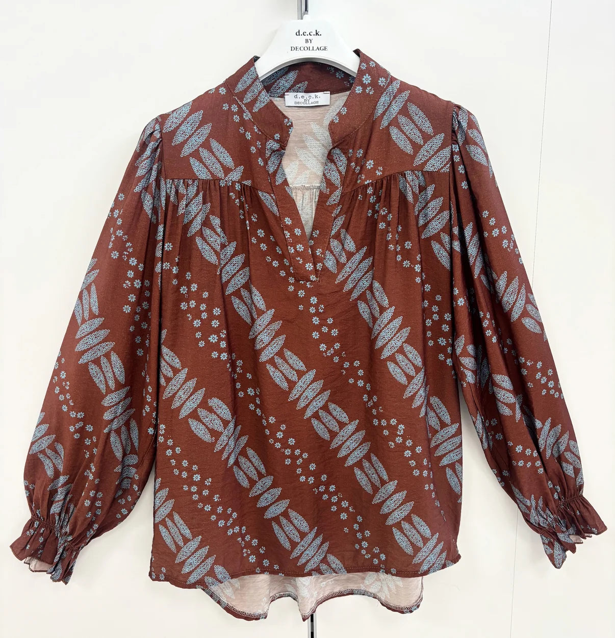 A brown long-sleeve blouse with a gray and white leaf block print pattern, hanging on a white hanger against a white background by Weirs Gifts