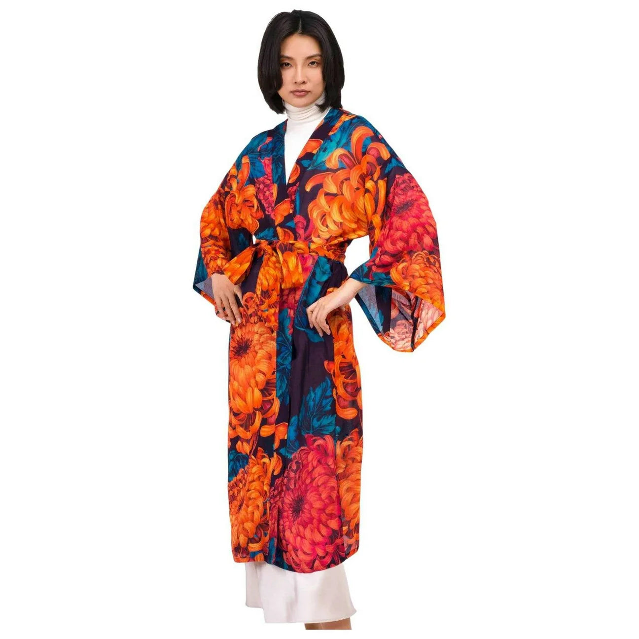 A model wearing a long-sleeved kimono-style robe with a vibrant orange, red, and teal floral print, styled over a white turtleneck and white pants against a solid white background by Weirs Gifts