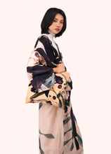 A model wearing a beige kimono-style robe with a dark purple and green floral print, styled over a white mock neck top, set against a solid pale pink background by Weirs Gifts