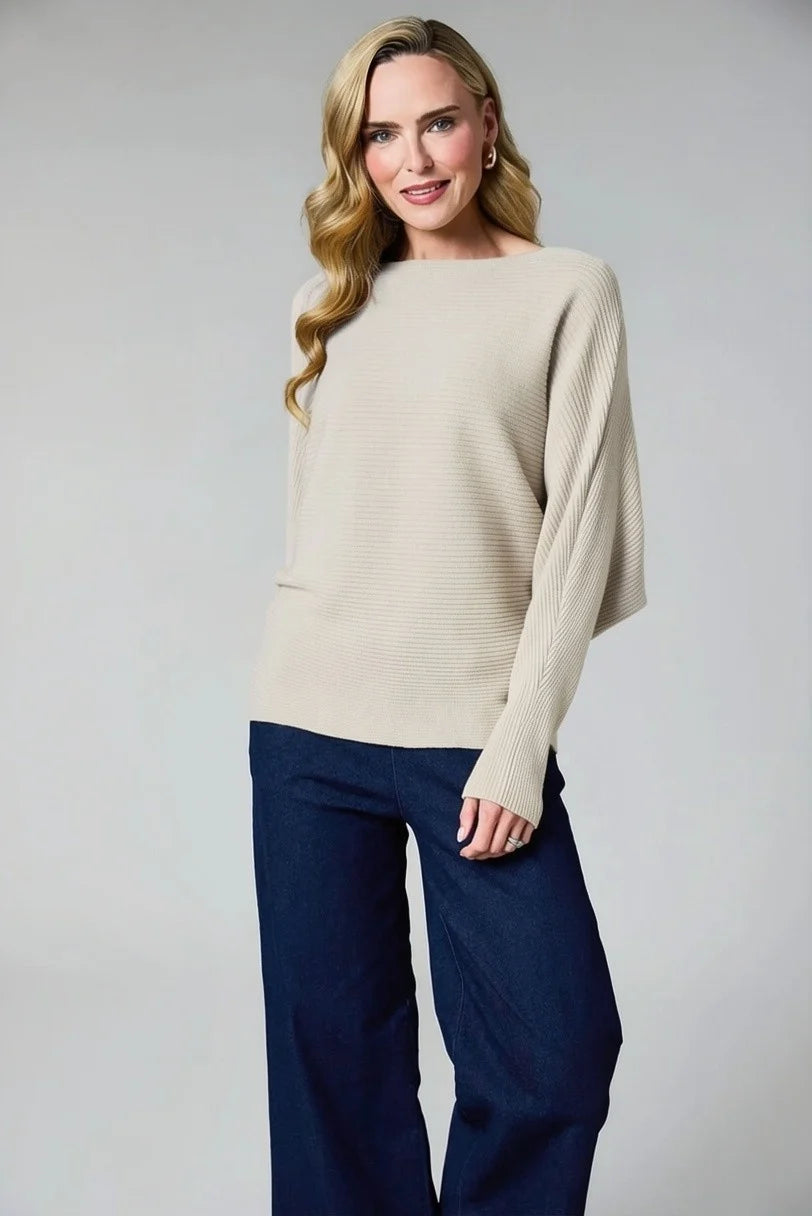 A woman modeling a cream ribbed knit sweater with wide sleeves and dark navy wide-leg pants, photographed against a neutral light gray studio background by Weirs Gifts