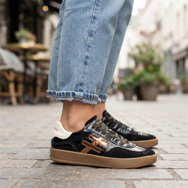A black leather low-top sneaker with a glossy patent finish, featuring a metallic bronze geometric logo on the side, a cream-colored heel tab with gold lettering, and a gum brown sole at Weirs Gifts
