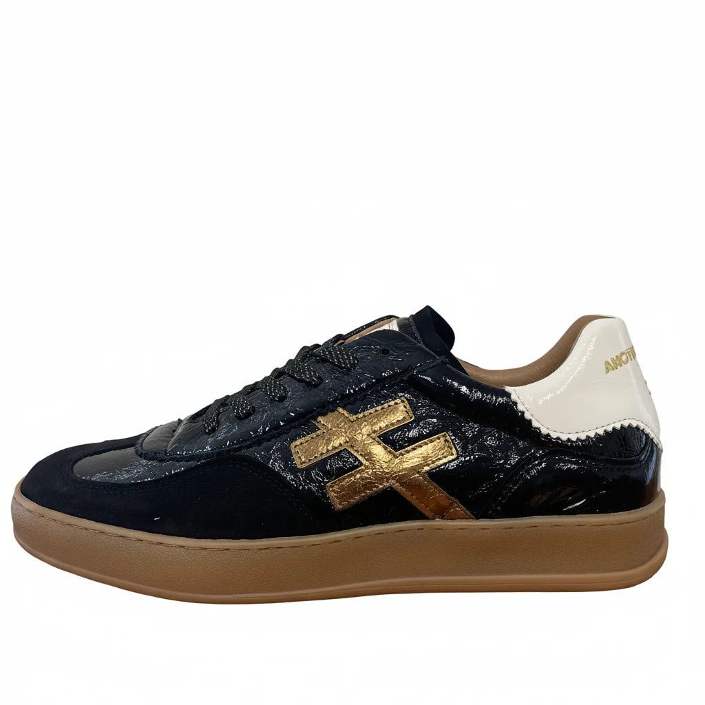 A black leather low-top sneaker with a glossy patent finish, featuring a metallic bronze geometric logo on the side, a cream-colored heel tab with gold lettering, and a gum brown sole at Weirs Gifts
