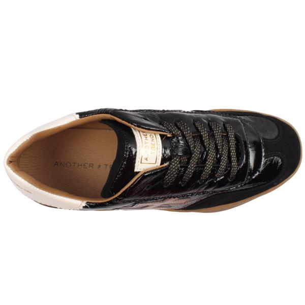A black leather low-top sneaker with a glossy patent finish, featuring a metallic bronze geometric logo on the side, a cream-colored heel tab with gold lettering, and a gum brown sole at Weirs Gifts