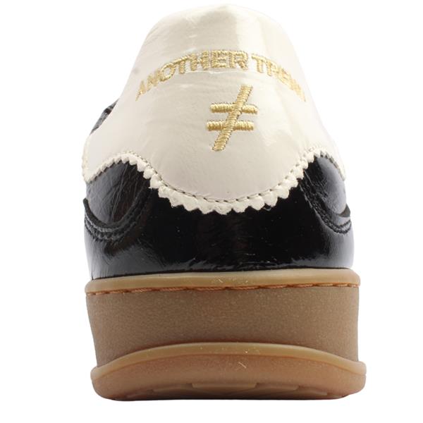 A black leather low-top sneaker with a glossy patent finish, featuring a metallic bronze geometric logo on the side, a cream-colored heel tab with gold lettering, and a gum brown sole at Weirs Gifts
