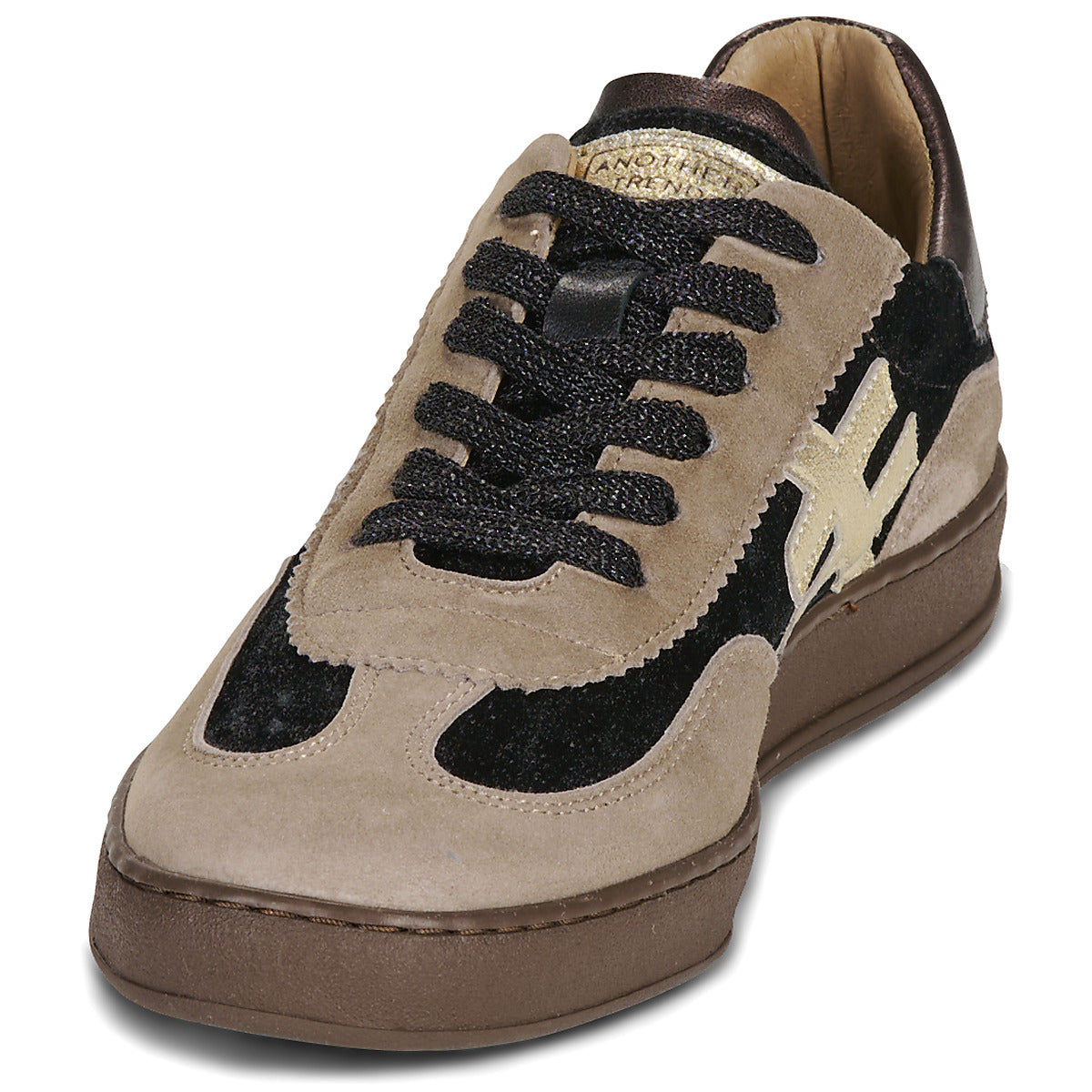 A low-top sneaker in beige suede and black suede, featuring black laces, a brown sole, and a gold-toned logo on the side at Weirs Gifts
