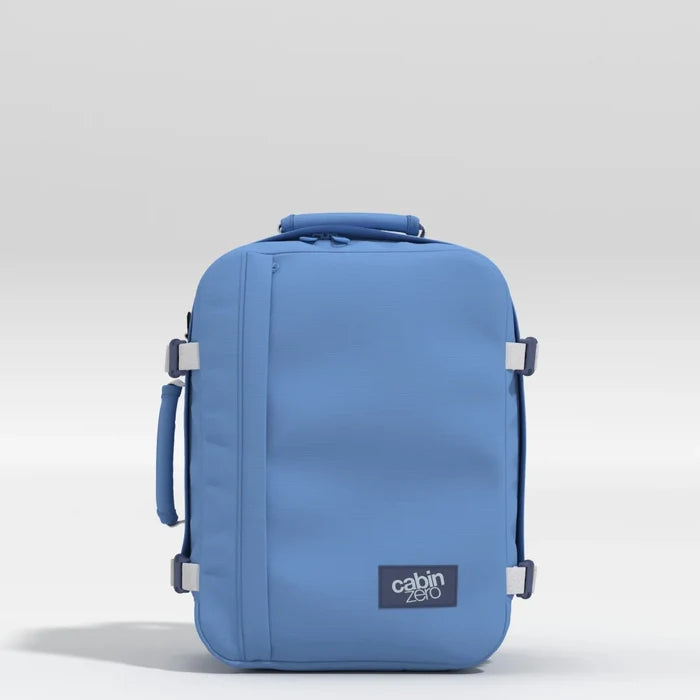 A blue Cabin Zero soft-sided rolling suitcase with a telescoping handle, side carry handles, and silver buckle details, set against a light gray studio background.