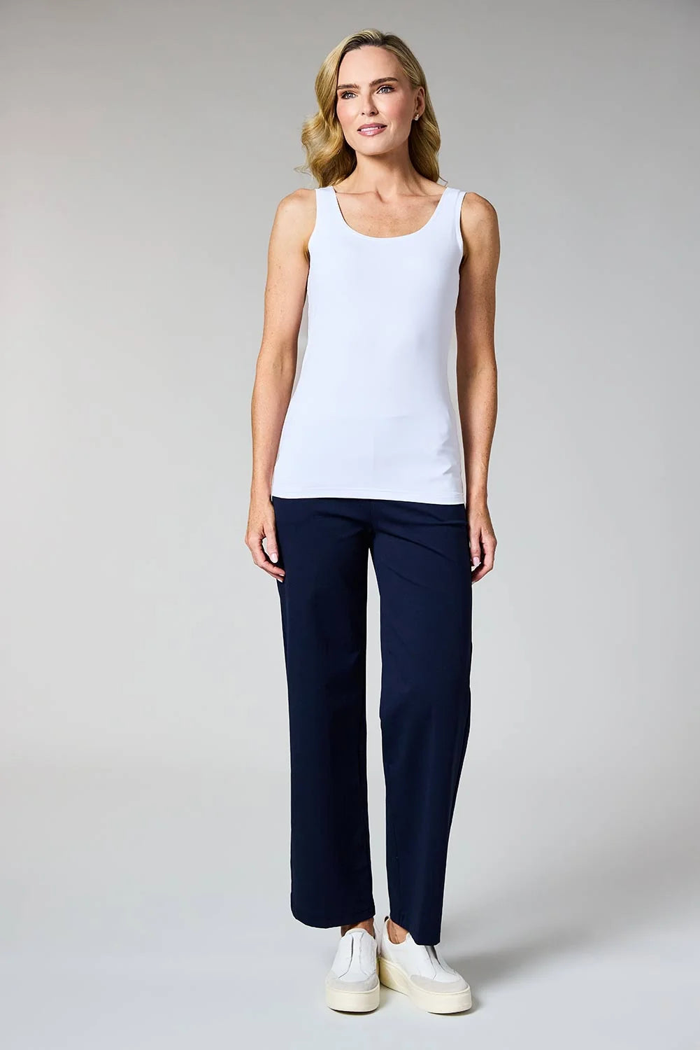 A woman modeling a white sleeveless tank top and navy blue wide-leg pants against a light gray studio background by Weirs Gifts