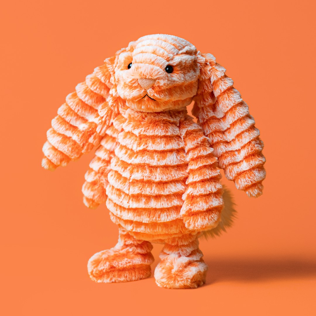An orange and white striped plush bunny toy with long floppy ears, standing against a solid orange background at Weirsgifts.ie