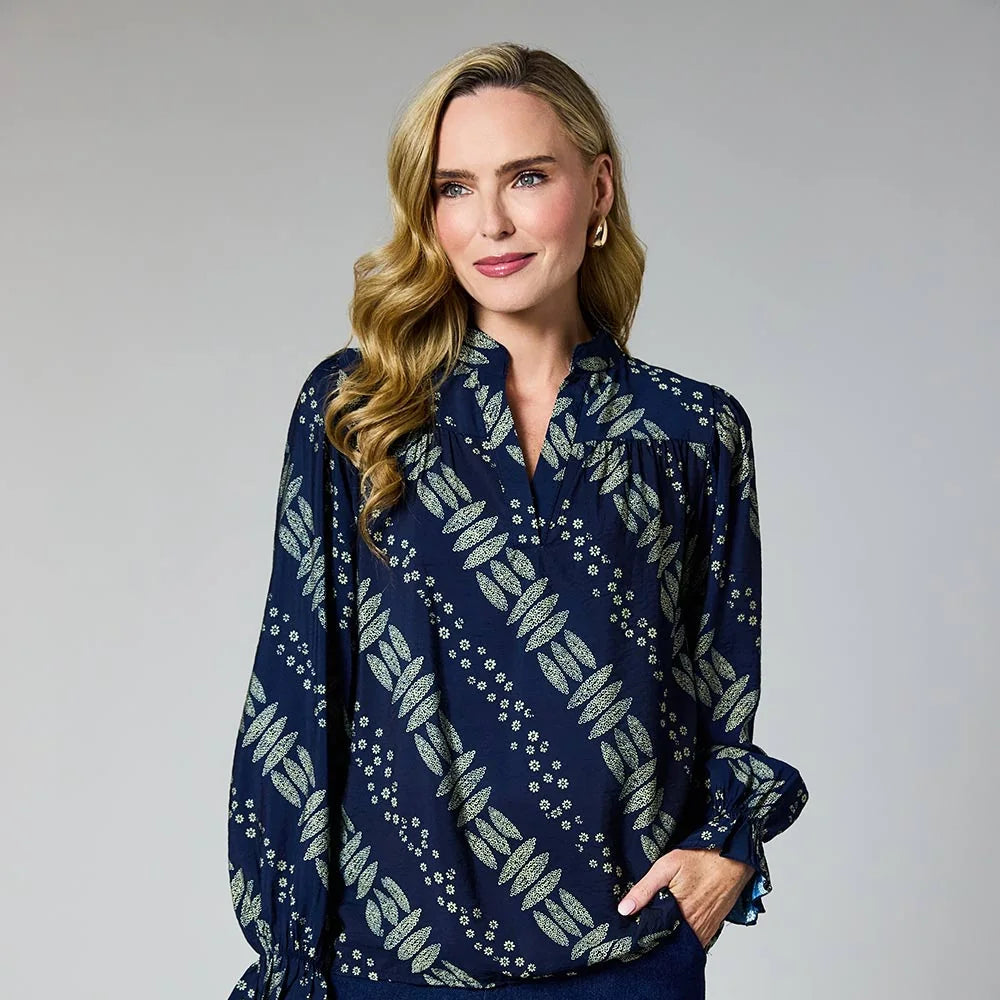 A woman modeling a navy blue long-sleeve blouse with a beige and white geometric pattern, paired with dark blue wide-leg pants, against a neutral gray studio background at Weirs Gifts
