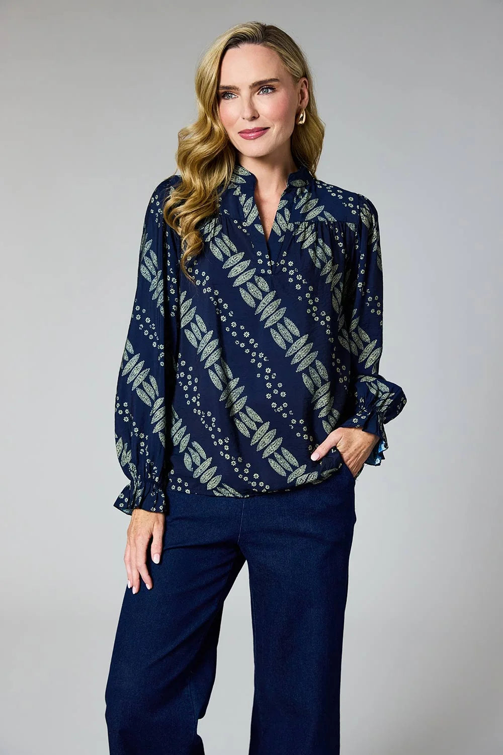 A woman modeling a navy blue long-sleeve blouse with a beige and white geometric pattern, paired with dark blue wide-leg pants, against a neutral gray studio background by Weirs Gifts