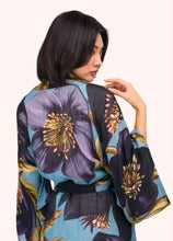 A woman shown from the back wearing a kimono-style robe with a large floral print in purple, teal, black, and gold on a plain light background by Weirs Gifts