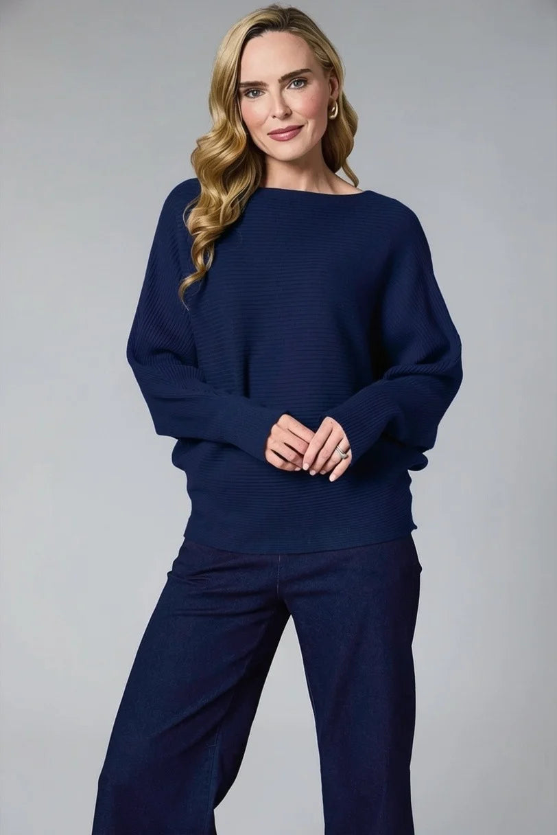 A woman modeling a navy blue ribbed knit sweater with a wide boat neckline and long sleeves, paired with matching navy wide-leg trousers, against a solid gray studio background by Weirs Gifts